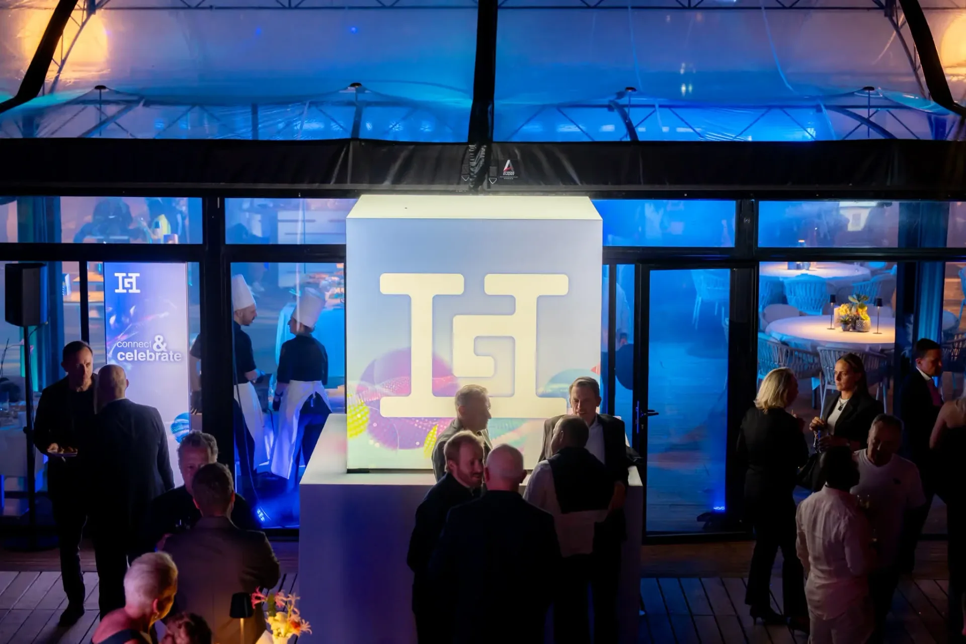Guests in front of the glowing cube with the Heinemann logo at the entrance of the Connect & Celebrate area, corporate gala evening at Palais Stéphanie Beach.