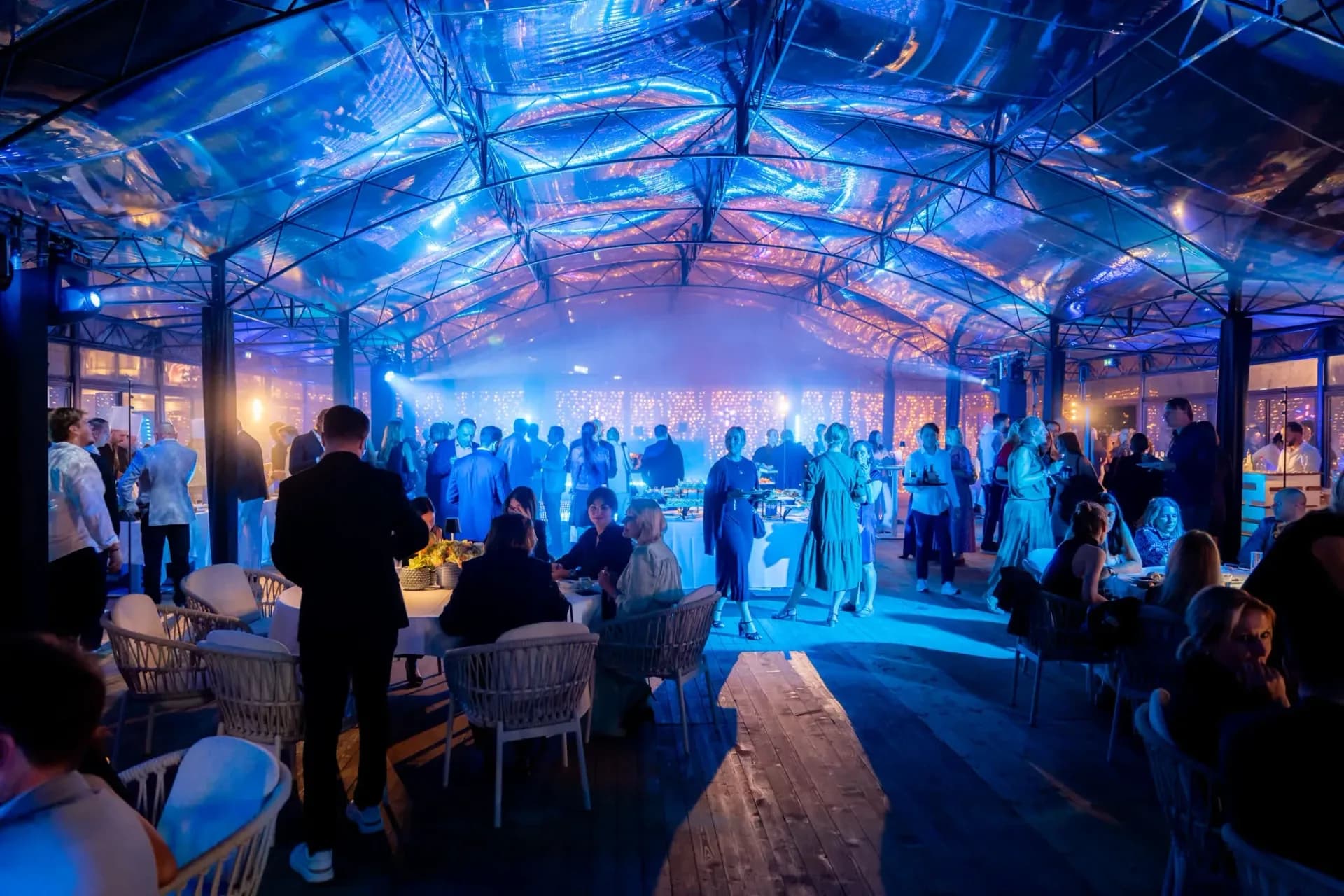 Inside the blue-lit glass roof of Palais Stéphanie Beach, guests around the buffet during the Gebr. Heinemann gala evening in Cannes.