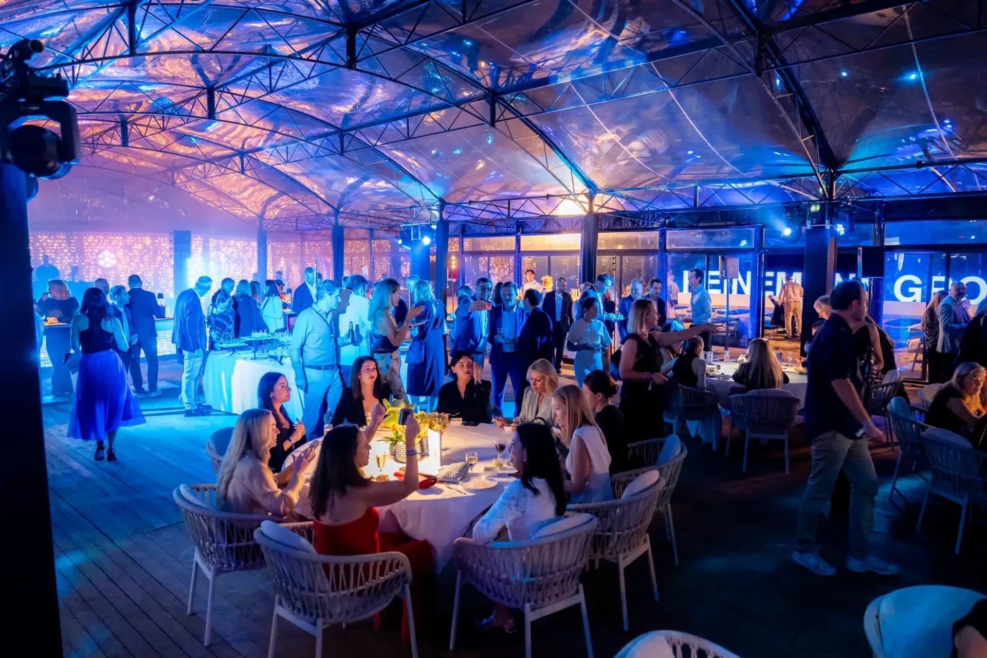 Dîner sous la verrière illuminée en bleu du Palais Stéphanie Beach à Cannes, tables d'invités lors de la soirée de gala Gebr. Heinemann, photographe événementiel.