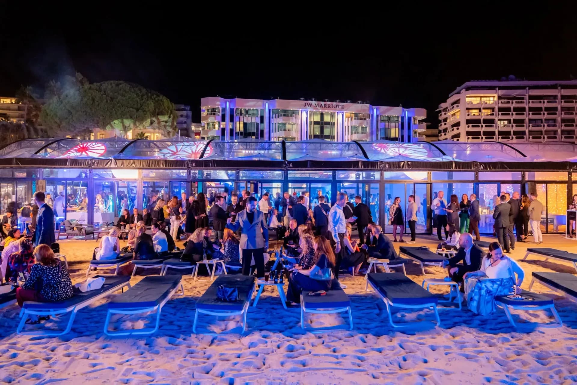 Transats alignés sur la plage face à la verrière du Palais Stéphanie Beach, espace Connect & Chill, soirée d'entreprise de nuit à Cannes.