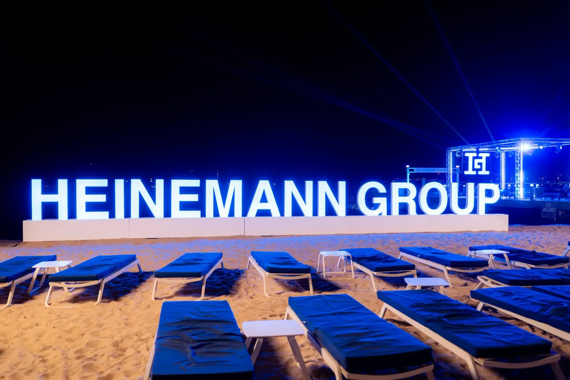 Lettres lumineuses Heinemann Group installées sur la plage de Cannes avec des transats bleus au premier plan, décor de la soirée de gala annuelle, photographe événementiel.