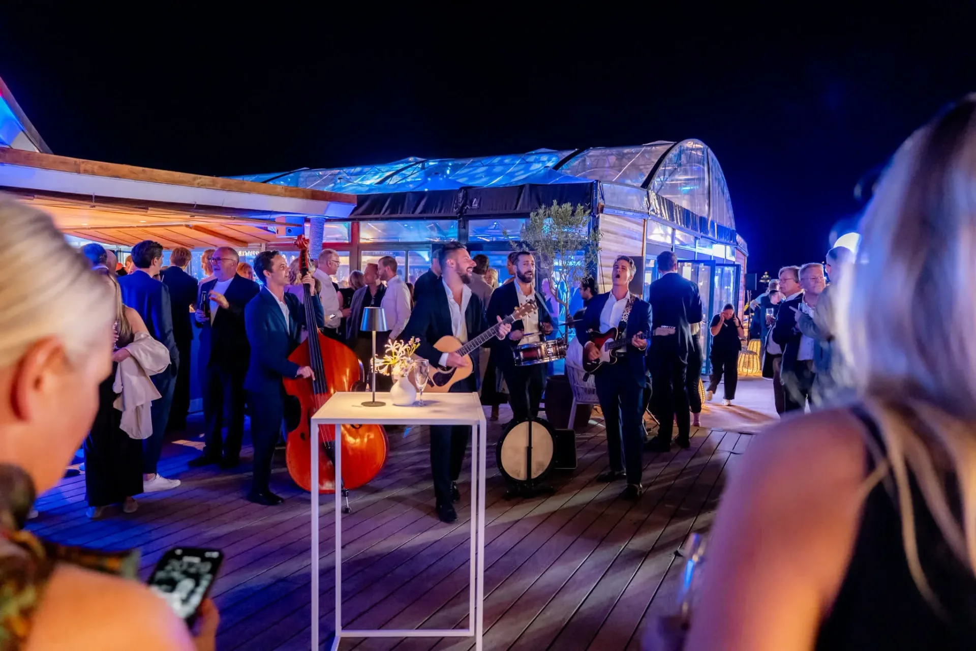 Musiciens jouant en live sur le deck du Palais Stéphanie Beach pendant la soirée de gala Heinemann à Cannes, invités en tenue de soirée, reportage photo événementiel.