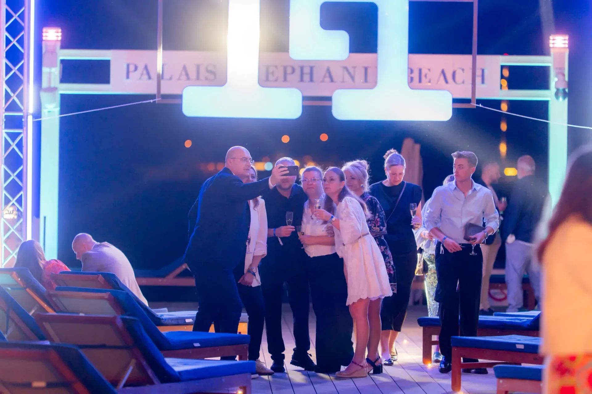 Invités de Gebr. Heinemann prenant un selfie sous l'enseigne Palais Stéphanie Beach à Cannes, photo de groupe spontanée lors d'une soirée de gala d'entreprise.