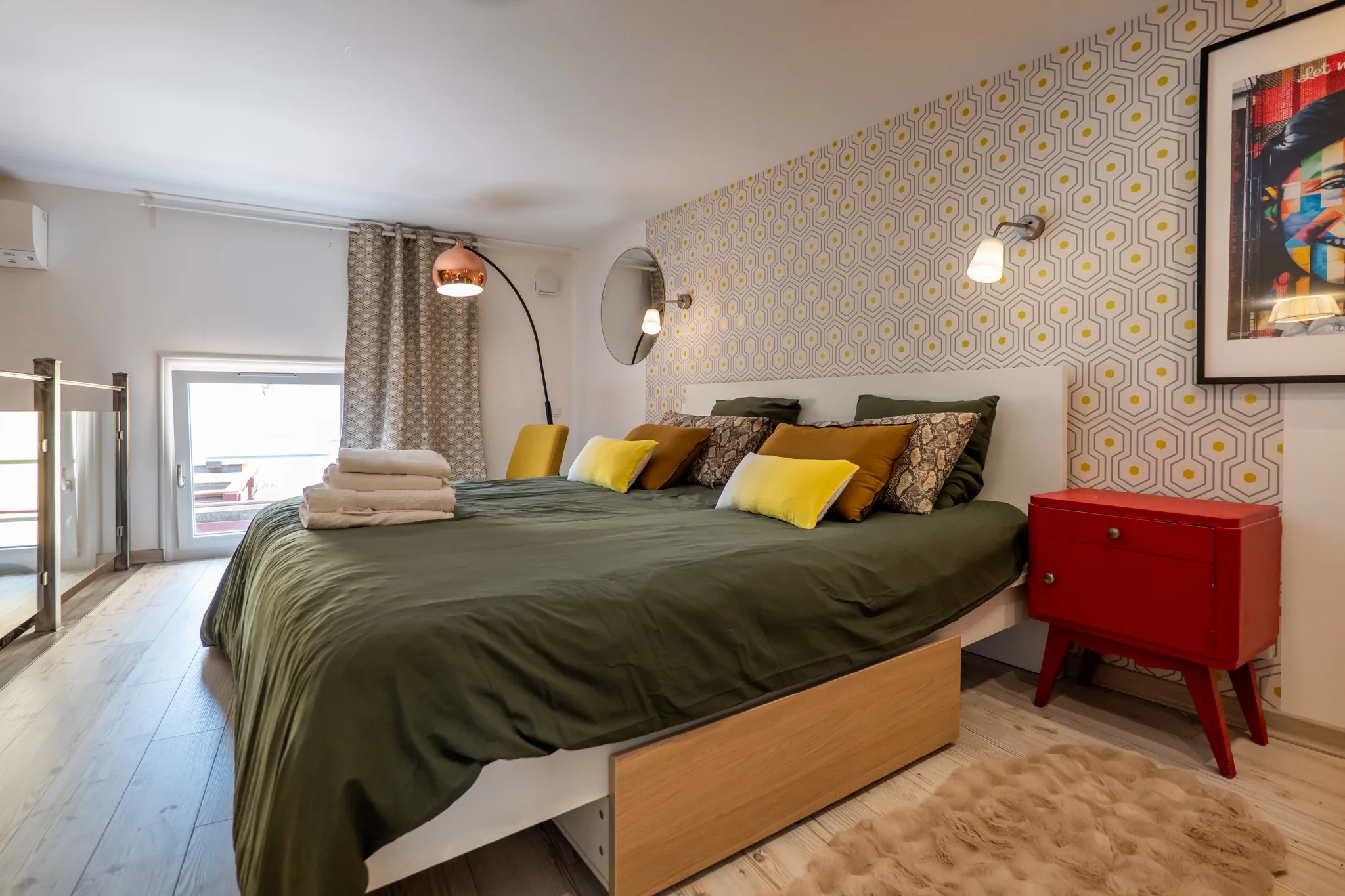 Chambre en mezzanine avec lit vert, papier peint graphique jaune et moutarde, décoration soignée.