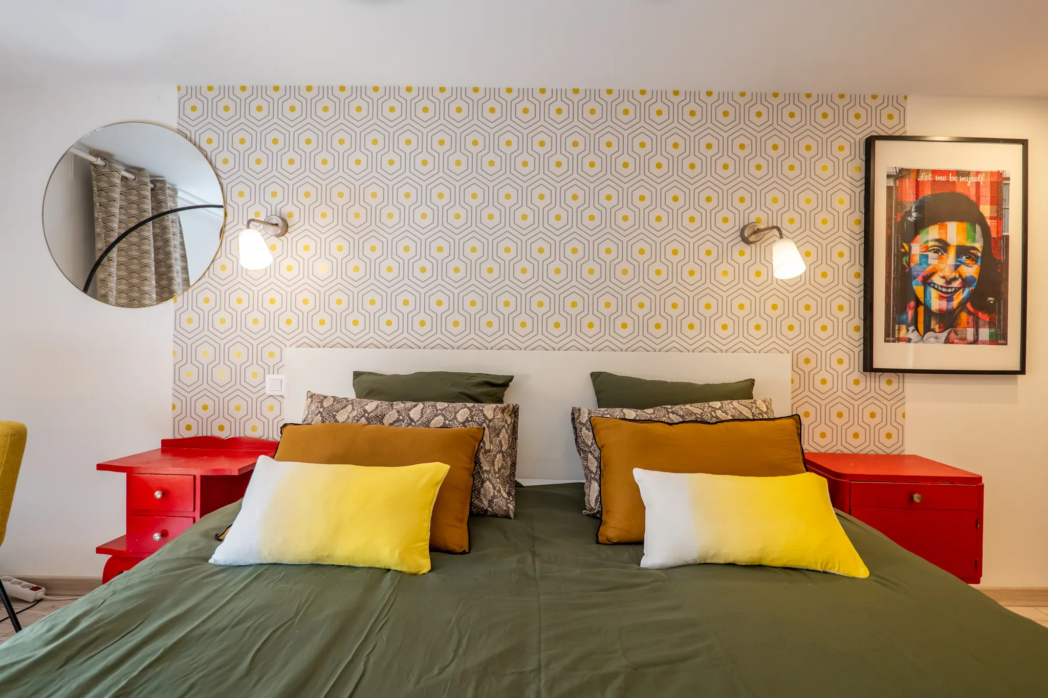 Chambre en mezzanine avec miroir rond, luminaire cuivré et fauteuil jaune moutarde.