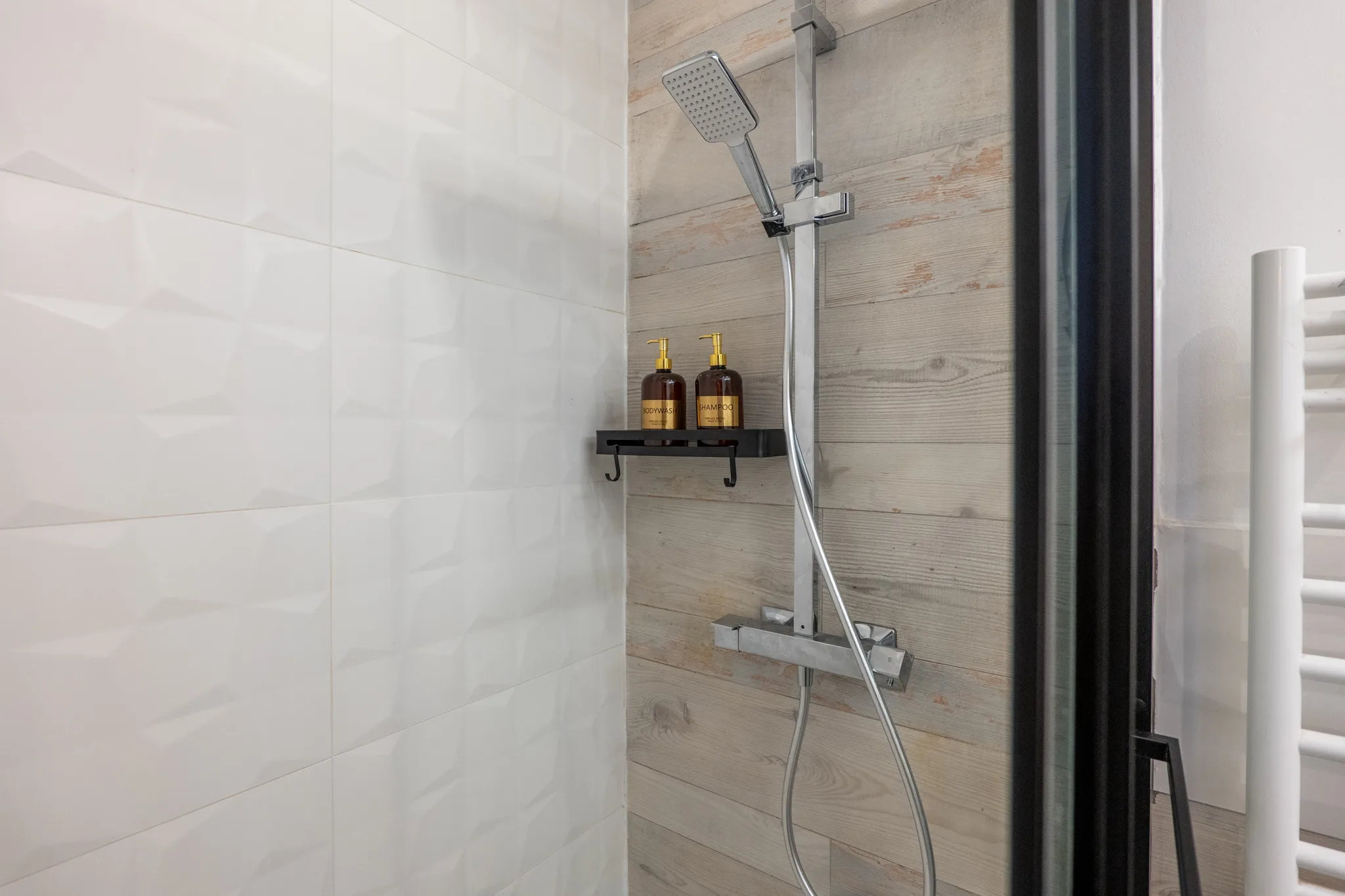 Détail de la douche à l'italienne avec bois patiné et produits d'accueil dans l'appartement à Manosque.