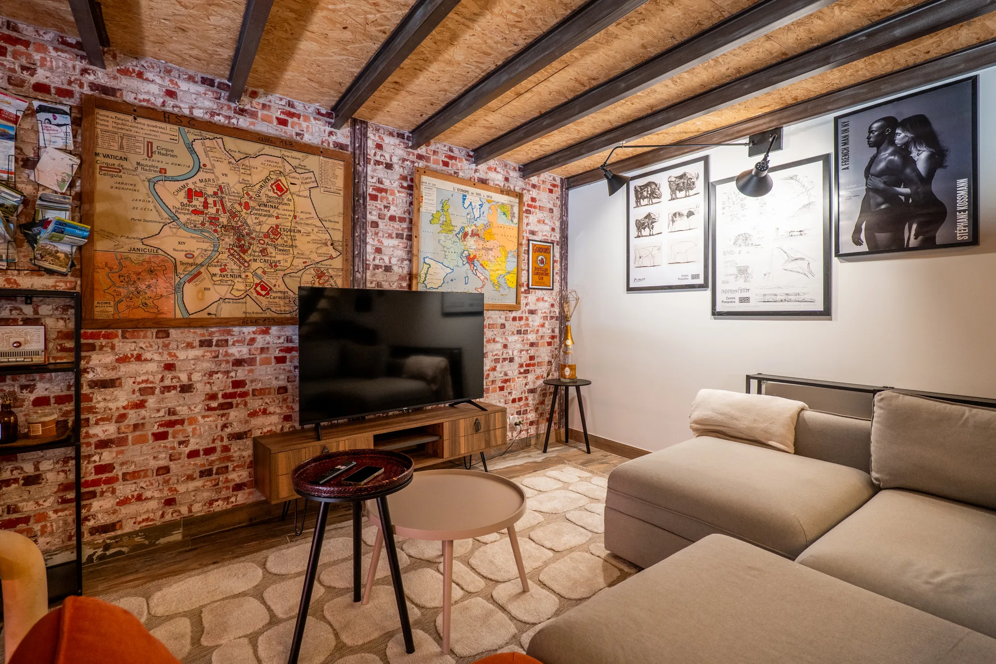 Salon cosy avec mur de brique rouge, canapé beige et galerie d'affiches d'art à Manosque.